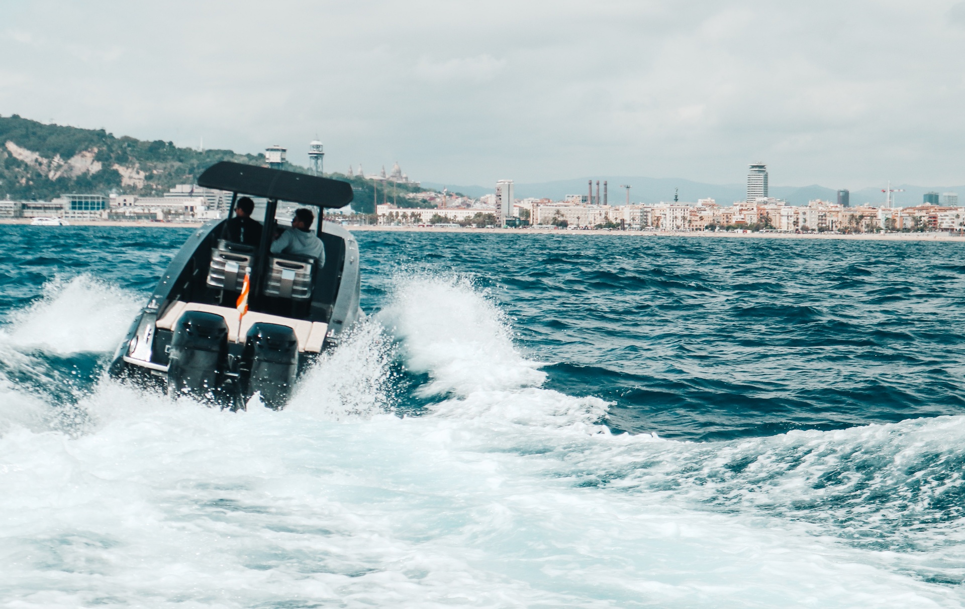 F11 seen from astern throwing a white wake across Barcelona water